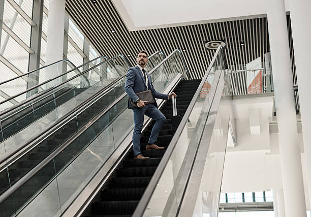 istock Confident Businessman Ascending Escalator in Modern Building with Briefcase 2218789619