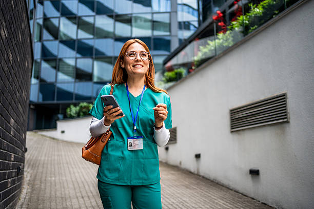 istock Smiling nurse walking and using smartphone near hospital 2218790359