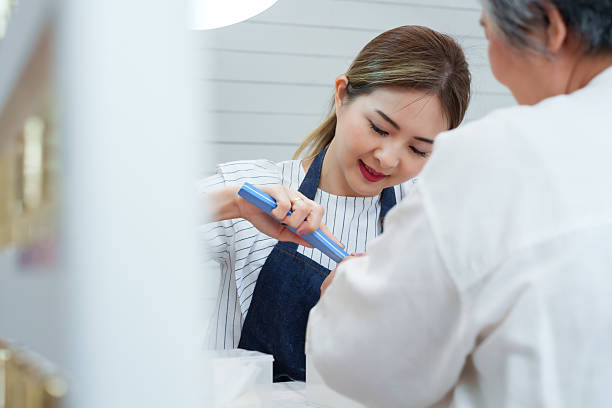 Friendly nail technician filing senior asian woman's nails during cozy professional manicure session beauty personal grooming hygiene wellness lifestyle relaxation customer care in small salon