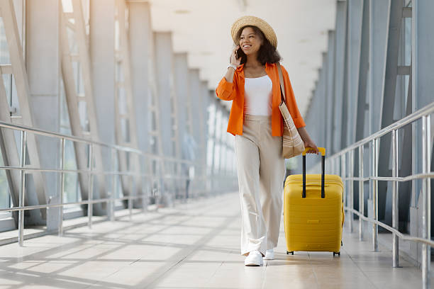istock Smiling Black Woman Talking On Cellphone While Walking With Suitcase In Airport 2218792730
