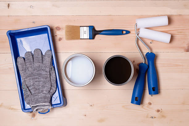 istock Choice of floor finish illustrated by two open cans with different coatings, rollers, brush, gloves and tray on wooden surface, renovation dilemma. 2218795836