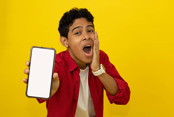 istock Young man with his hand on his face, surprised, showing his cell phone with blank space for advertising space on a yellow background 2218797872