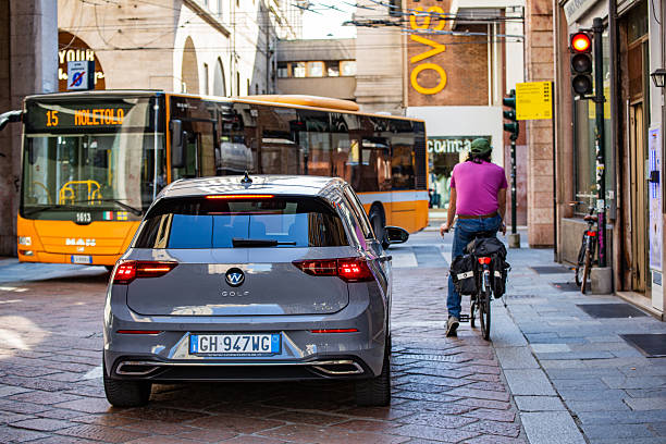 Parma, Italy, April 4, 2025: Volkswagen Golf in urban traffic next to a cyclist and city bus in Italy.