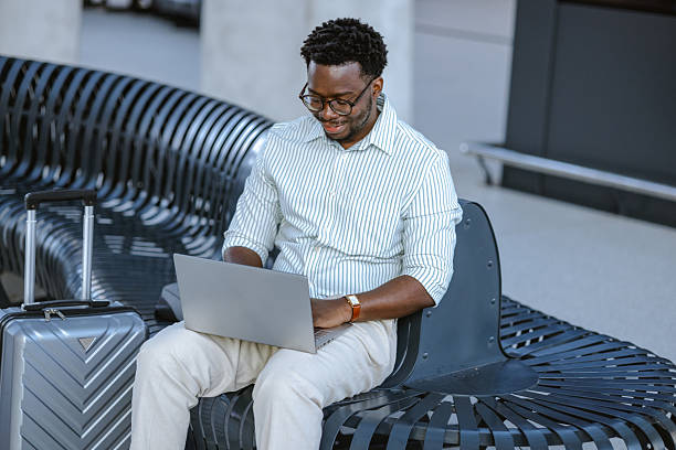 istock Professional man using laptop on bench at public station with suitcase nearby 2218800036