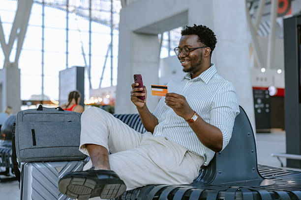 istock Smiling man using smartphone and credit card at a modern transportation hub 2218801011