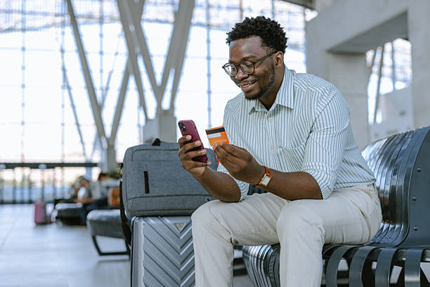 istock Smiling man using smartphone and credit card at a modern transportation hub 2218801070