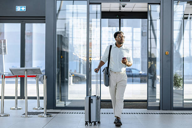 istock Smiling traveler pulling suitcase and holding a smartphone at modern transportation terminal 2218801294