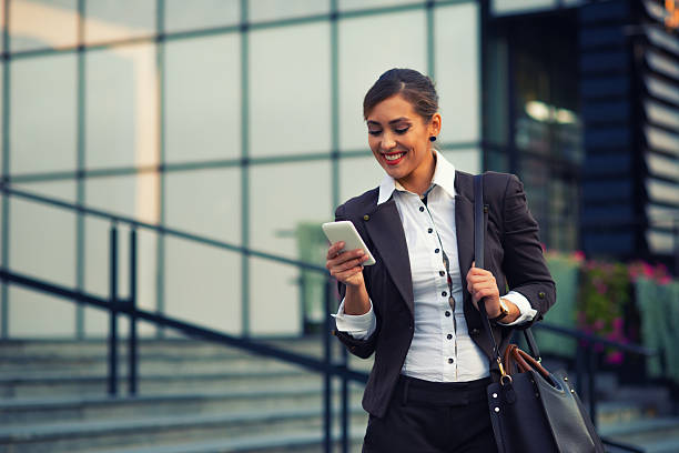 istock Young smiling female entrepreneur using phone in front of her office building 2218803547