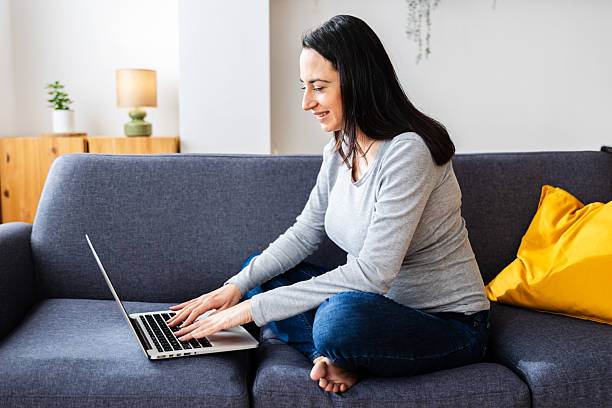 istock Young happy woman using laptop computer sitting on sofa at home 2218804885