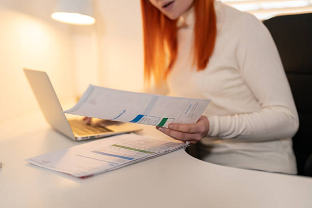istock Woman reviewing documents while working on a laptop in a well-lit home office during the day 2218808541