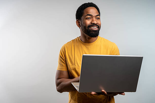 istock Young man standing holding laptop and looking at camera with happy smile 2218809556