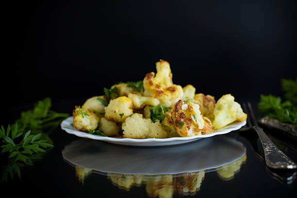 Fried cauliflower with spices and herbs on a black background.