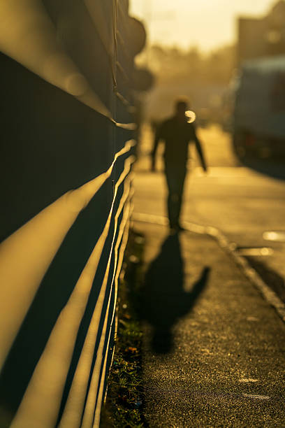 istock Silhouetted man walking along sunlit street at dusk. 2218816551
