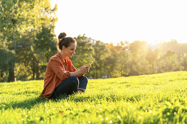 istock Modern woman sitting on the grass and texting message using her smartphone. 2218820667