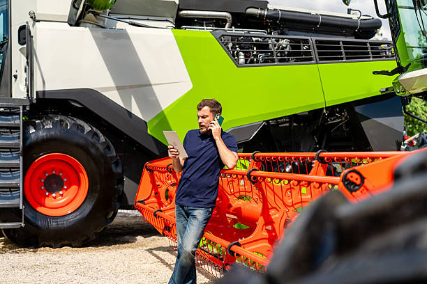 istock Agriculture industry worker using tablet and speaking on mobile phone near tractor 2218820984