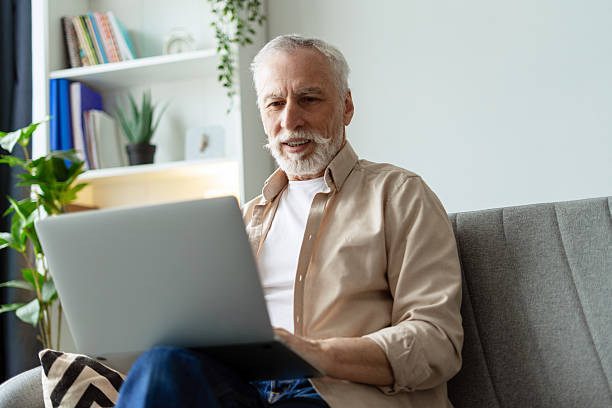istock Senior man using laptop sitting on sofa at home 2218823020
