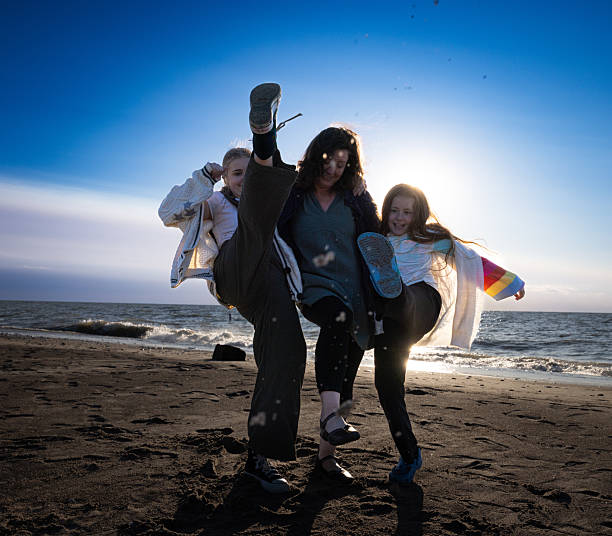 A mother and her two daughters laugh and walk on the beach during early evening