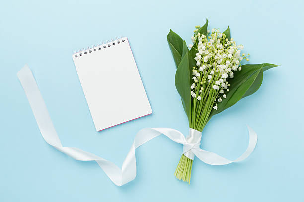 Lilies of the valley with notebook on color background, top view