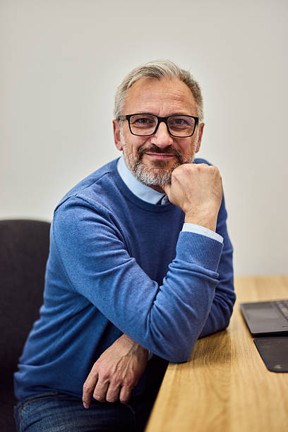 istock Confident Senior Man in Office Setting Wearing Blue Sweater and Glasses 2218829735