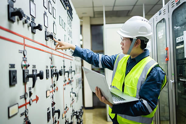 istock Electrical engineer is performing inspection in substation control room with control panel while holding laptop and wearing safety gear for precise monitoring and control 2218849153