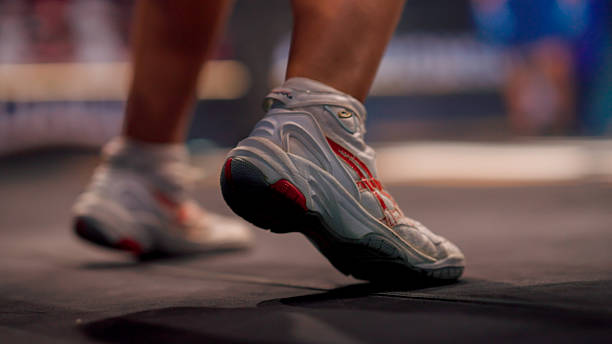 Close-up view of a woman tying shoelaces on a sneaker while sitting on a couch indoors. The casual setting and focus on hands emphasize preparation, daily routine, or an active lifestyle. Natural light and warm tones add a cozy and authentic atmosphere.