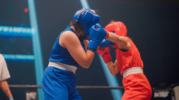 Two young female boxers punching and blocking each other during a fighting match in a stadium.