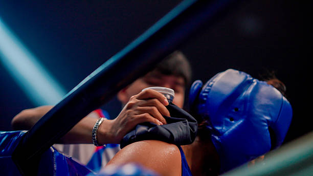 A boxing crew member using a towel to wipe sweat from a young female boxer while resting between rounds.