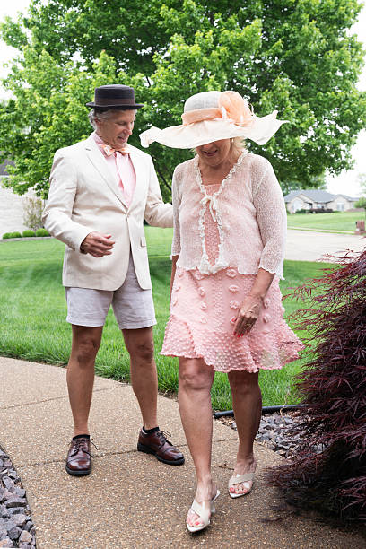 Male and female couple in 60's dress up for a Kentucky Derby party wearing hats and stand outside on a sidewalk at their home, Indiana