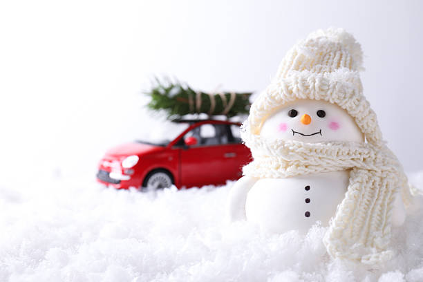 istock Cute decorative snowman and toy car with fir tree branches on artificial snow against light background, selective focus 2218859852