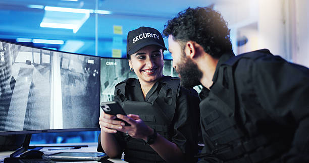 istock Happy people, security guard and night with phone for surveillance or supervision at protection agency. Man, woman or officers working late with smile on mobile smartphone for safety in control room 2218866251
