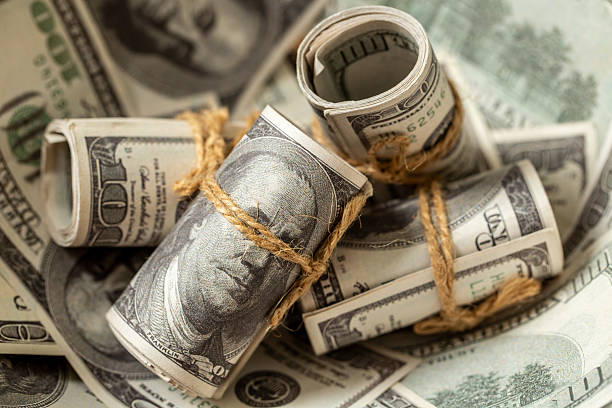 A detailed close-up of tightly rolled bundles of US dollar banknotes, suggesting accumulated wealth or savings. However, in the context of inflation, this image subtly conveys the idea that even significant amounts of money can lose their real value over time. It represents the quiet erosion of purchasing power, making it a compelling visual for discussions on long-term financial planning, investment strategies, the impact of rising prices on accumulated capital, and the challenge of preserving wealth in an inflationary economy.