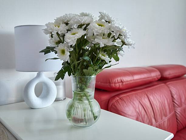 istock Vase of white chrysanthemums sits on a table next to a lamp 2218870444