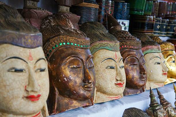 A collection of ornate Buddha head sculptures in a market display, showcasing intricate details and vibrant colors.