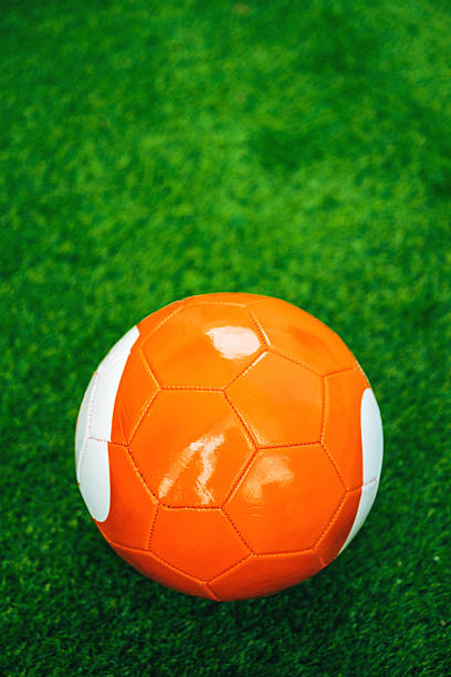 Orange soccer ball on artificial grass pitch, selective focus