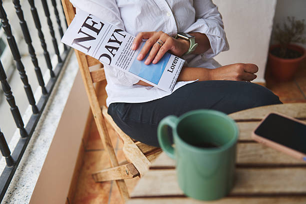 istock Woman Relaxing Outdoors with Newspaper, Coffee Mug, and Smartphone on a Rustic Balcony 2218880651