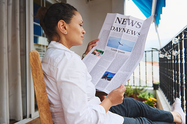istock Woman Relaxing on Balcony While Reading a Newspaper in Natural Light 2218880660