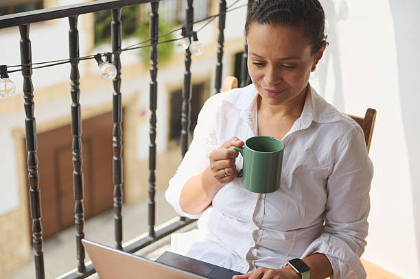 istock Woman Sitting on Balcony Holding Mug While Using Laptop for Work or Relaxation 2218880665