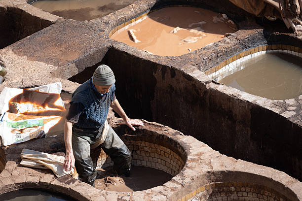 A worker tending to leather tanning pits in a traditional Moroccan tannery in Fes. Vibrant hues and textures showcase the intricate artisanal craftsmanship preserved in this centuries-old industry.