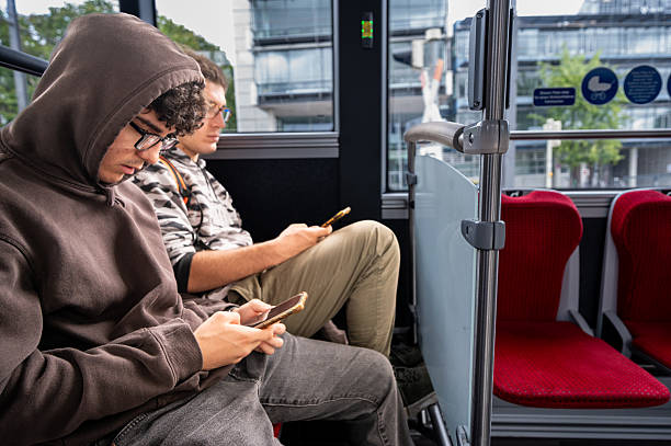 istock Two young people sitting on the bus talking using their cell phones. Concept of technology use by young people. 2218884741
