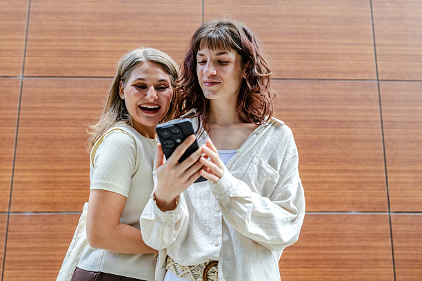 istock Two young women enjoy time together while texting and smiling outdoors, sharing moments of friendship and excitement over their smartphones 2218887628