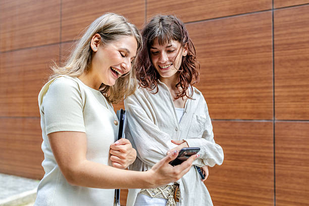 istock Two young women enjoy sharing excitement together while using their smartphones outdoors in a modern setting 2218887784