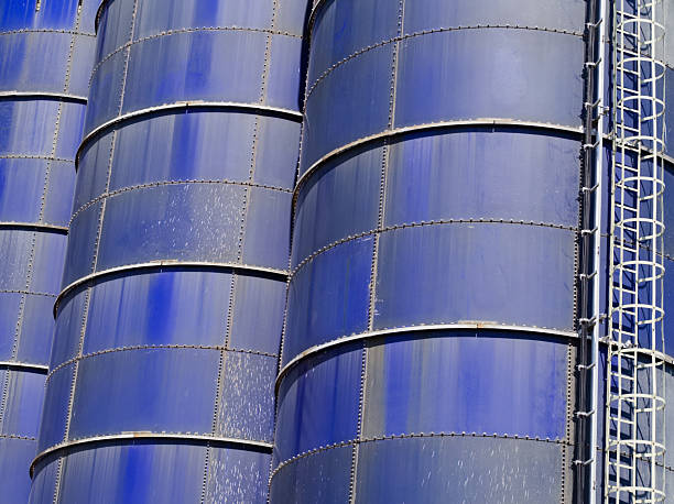 Blue on blue industrial area with three cylandrical tanks behind barbed wire fence.