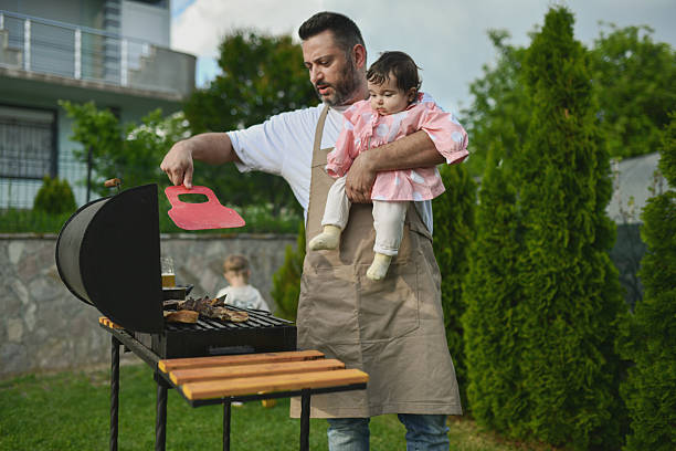 istock Tender Father Holding Baby Daughter While Cooking Barbecue Outside 2218921520