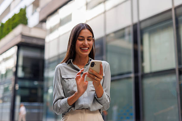 istock Professional businesswoman texting, smiling while walking past modern corporate office exterior 2218922204