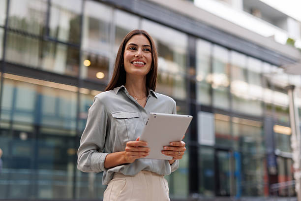 istock Professional female entrepreneur walking confidently near corporate headquarters, using digital tablet and embodying modern business success 2218922238