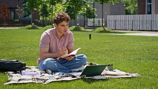istock Online student video calling laptop sitting green grass park. Relaxed man 2218931876