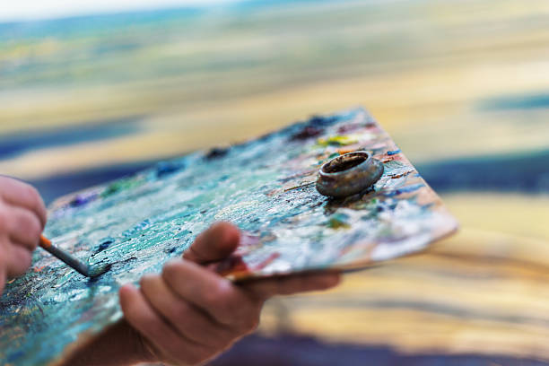 Close-up of a painter's hand picking up blue color with a brush from a palette