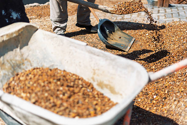 Construction worker shoveling gravel into a wheelbarrow on a sunny day