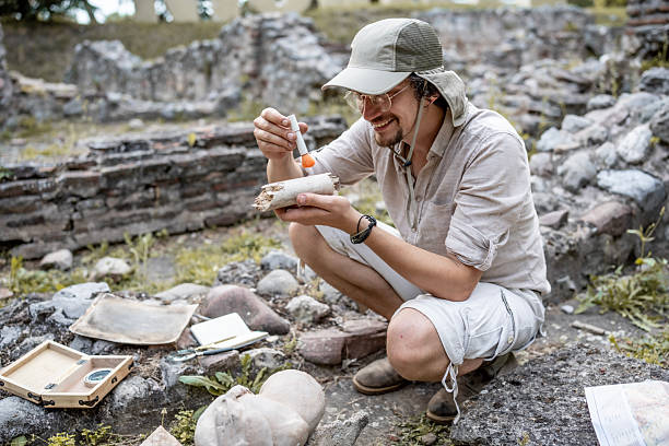 A researcher uses tools to study and analyze an ancient bone at an archaeological site, showcasing focus and meticulous attention at an outdoor excavation location enveloped in natural surroundings.
