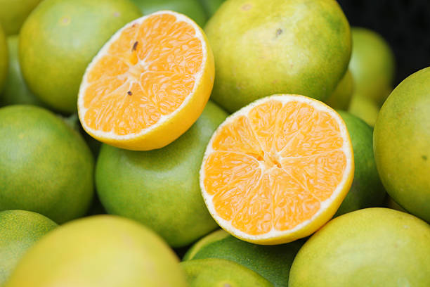 Halved oranges sit among whole green oranges at a bustling market.